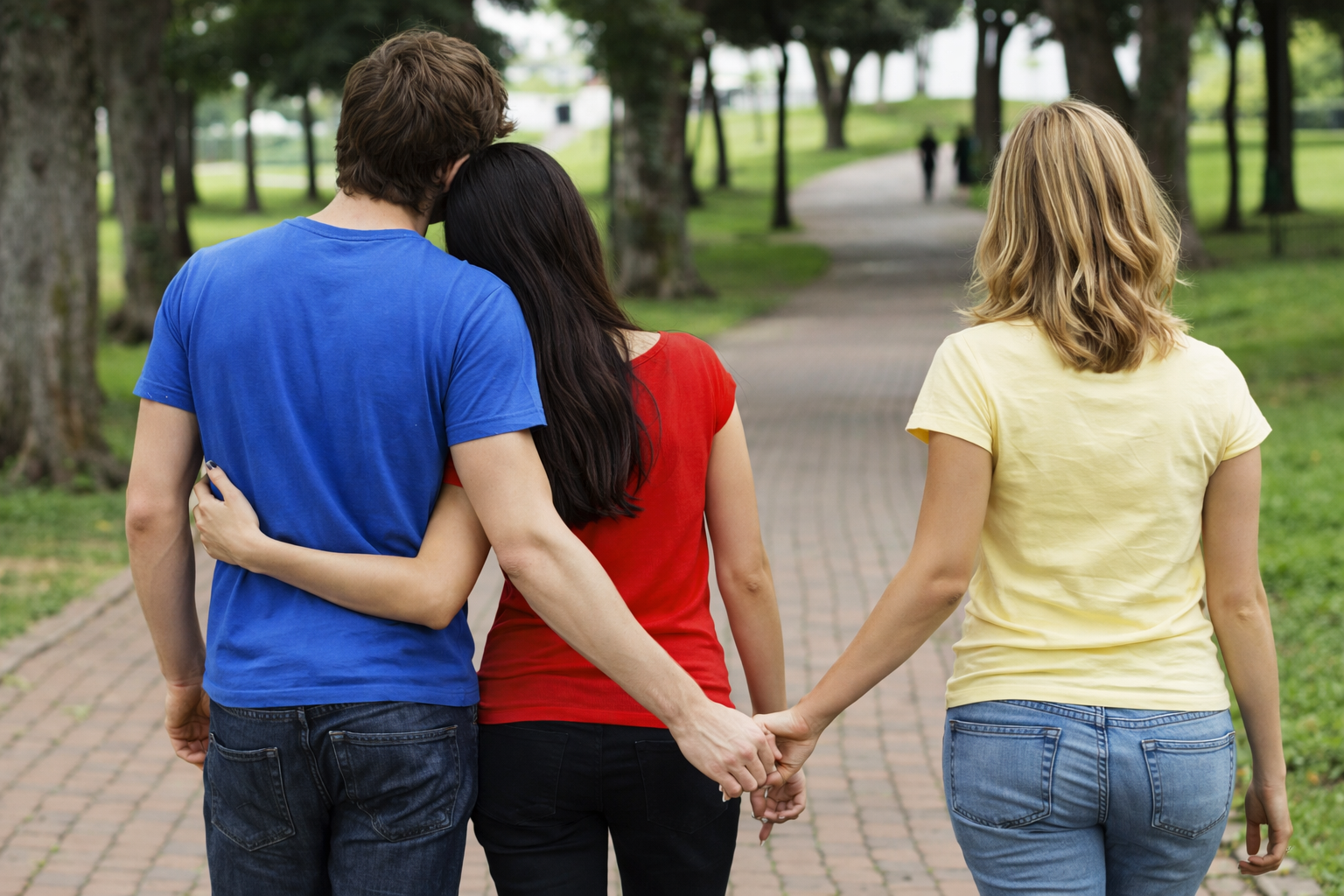 couple marchant ensemble dans un parck avec l'homme qui tient discretement la main d'une autre femme